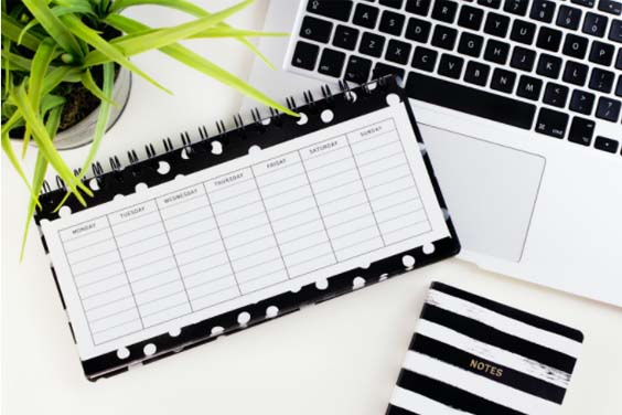 A weekly planner next to a laptop